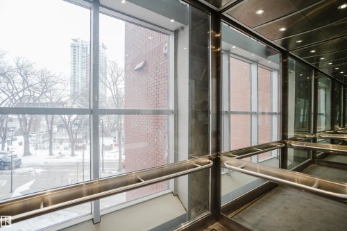 The property offers a modern elevator with clear glass panels, providing views of the surrounding neighborhood and a nearby brick building - 206 10108 125 Street, Edmonton, AB - Indoor Photo Showing Other Room