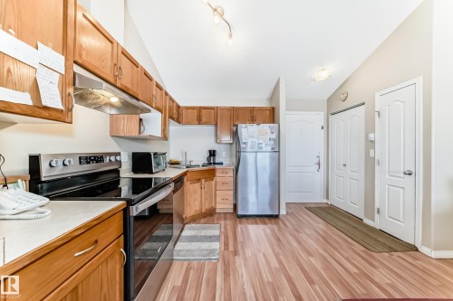 The kitchen features wood cabinetry, a stainless steel electric range, and a stainless steel refrigerator - 324 9525 162 Avenue Nw, Edmonton, AB - Indoor Photo Showing Kitchen