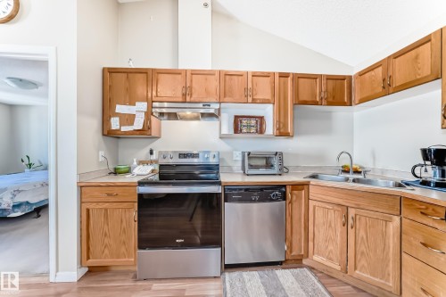 The kitchen features wood cabinetry, a stainless steel oven and dishwasher, a double basin sink, and laminate countertops - 324 9525 162 Avenue Nw, Edmonton, AB - Indoor Photo Showing Kitchen With Double Sink
