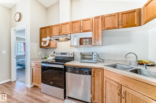 The kitchen features wooden cabinetry, a stainless steel oven and dishwasher, and a double basin sink - 324 9525 162 Avenue Nw, Edmonton, AB - Indoor Photo Showing Kitchen With Double Sink