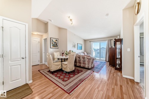 The open concept living area features light wood flooring, vaulted ceilings, and a sliding glass door leading to a balcony - 324 9525 162 Avenue Nw, Edmonton, AB - Indoor
