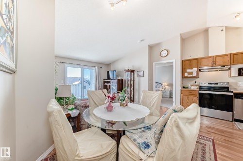 Open concept living area featuring a kitchen with wood cabinetry and stainless steel appliances, a dining area with a glass-top table, and a living room with access to a sliding glass door - 324 9525 162 Avenue Nw, Edmonton, AB - Indoor