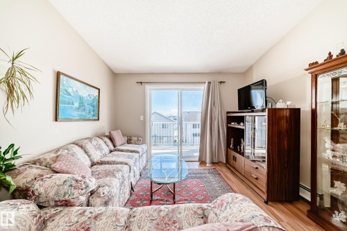 The living area features hardwood flooring, a sliding glass door leading to the outdoors, and a decorative rug - 324 9525 162 Avenue Nw, Edmonton, AB - Indoor Photo Showing Living Room
