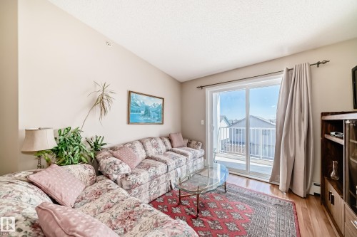 Living room featuring hardwood flooring, a vaulted ceiling, and a sliding glass door providing access to a private balcony - 324 9525 162 Avenue Nw, Edmonton, AB - Indoor Photo Showing Living Room