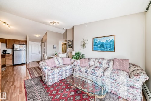 Living area featuring light wood flooring, track lighting, and a red patterned area rug - 324 9525 162 Avenue Nw, Edmonton, AB - Indoor Photo Showing Living Room