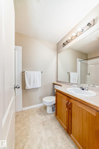 The bathroom features a wooden vanity with a white countertop and an integrated sink, a large mirror with overhead lighting, a toilet, and tiled flooring - 324 9525 162 Avenue Nw, Edmonton, AB - Indoor Photo Showing Bathroom