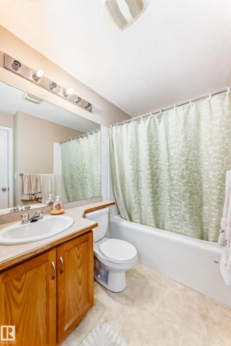 Bathroom featuring a vanity with a light wood base and an integrated sink, a toilet, and a bathtub with a shower curtain - 324 9525 162 Avenue Nw, Edmonton, AB - Indoor Photo Showing Bathroom