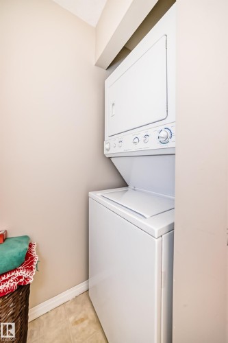 Laundry area featuring a stacked washer and dryer unit, beige walls, and tiled flooring - 324 9525 162 Avenue Nw, Edmonton, AB - Indoor Photo Showing Laundry Room