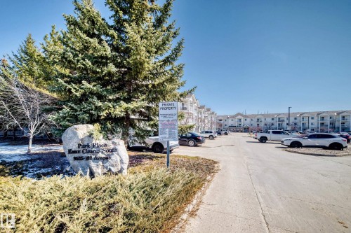 The property features a large parking area, manicured landscaping with evergreen trees and shrubs, and a stone sign - 324 9525 162 Avenue Nw, Edmonton, AB - Outdoor