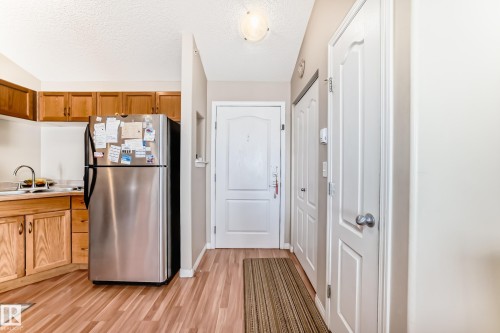 The property features a kitchen area with light wood cabinetry, a stainless steel refrigerator, and a sink with a chrome faucet - 324 9525 162 Avenue Nw, Edmonton, AB - Indoor Photo Showing Kitchen