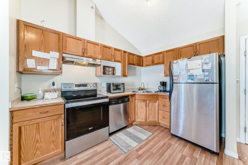 The kitchen features wood cabinetry, light countertops, and stainless steel appliances, including a refrigerator, stove, and dishwasher - 324 9525 162 Avenue Nw, Edmonton, AB - Indoor Photo Showing Kitchen With Double Sink
