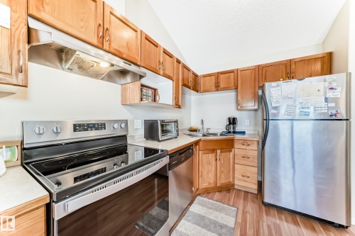 The kitchen features wood cabinetry, light-colored countertops, and stainless steel appliances including a range, dishwasher, and refrigerator - 324 9525 162 Avenue Nw, Edmonton, AB - Indoor Photo Showing Kitchen With Double Sink