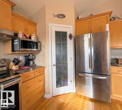 Well-appointed kitchen featuring hardwood floors, light-toned wooden cabinetry, a stainless steel refrigerator, and a door with frosted glass panels - 16832 79 Street Nw, Edmonton, AB - Indoor Photo Showing Kitchen
