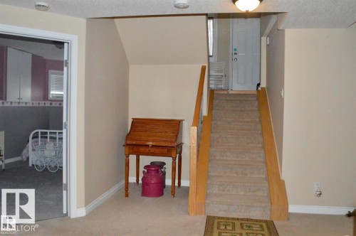 This area features light-colored walls and carpeted flooring, with a carpeted staircase leading to a white door - 16832 79 Street Nw, Edmonton, AB - Indoor Photo Showing Other Room