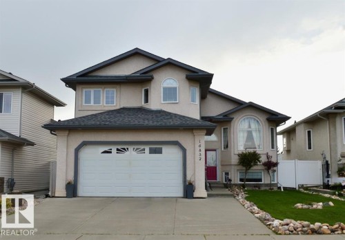 The property features a stucco exterior, a two-car garage with a concrete driveway, and a red front door - 16832 79 Street Nw, Edmonton, AB - Outdoor With Facade