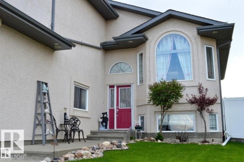 The property features an exterior with light-colored stucco siding, dark eaves, and a prominent arched window on the upper level - 16832 79 Street Nw, Edmonton, AB - Outdoor With Facade
