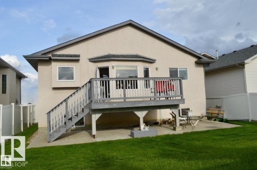 The property features a stucco exterior, a raised deck with railing and stairs, and a concrete patio beneath the deck - 16832 79 Street Nw, Edmonton, AB - Outdoor With Deck Patio Veranda