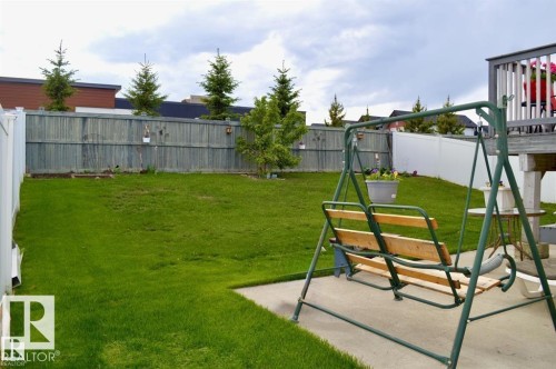 The property features a spacious backyard with a well-maintained lawn, a wooden fence, and mature evergreen trees - 16832 79 Street Nw, Edmonton, AB - Outdoor With Backyard