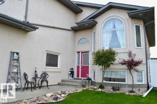 The property features a stucco exterior, a prominent arched window, and a vibrant red entrance door - 16832 79 Street Nw, Edmonton, AB - Outdoor