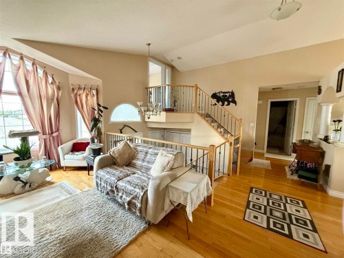 The property features hardwood flooring throughout this bright living area, which includes a staircase with wooden handrails and metal balusters - 16832 79 Street Nw, Edmonton, AB - Indoor Photo Showing Living Room