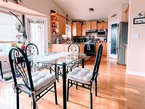 The property features a bright kitchen and dining area with hardwood floors, natural wood cabinetry, and a door with a decorative glass insert - 16832 79 Street Nw, Edmonton, AB - Indoor Photo Showing Dining Room