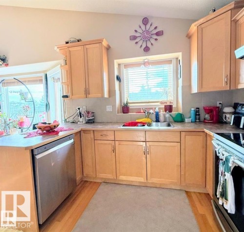 The kitchen features light wood cabinetry, a stainless steel dishwasher, and a window above the sink - 16832 79 Street Nw, Edmonton, AB - Indoor Photo Showing Kitchen