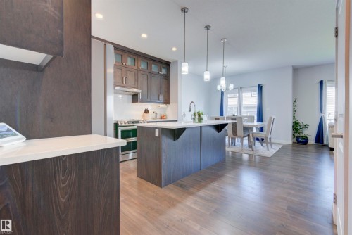 The kitchen features dark wood cabinetry, light countertops, and a central island with a sink - 8452 Cushing Crest, Edmonton, AB - Indoor Photo Showing Kitchen With Upgraded Kitchen