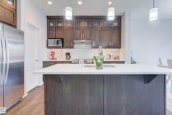 The kitchen features dark wood cabinetry, a stainless steel refrigerator, and a kitchen island with a white countertop - 