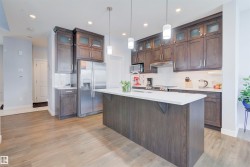 Modern kitchen featuring a large central island with a white countertop, recessed lighting, and pendant lights - 
