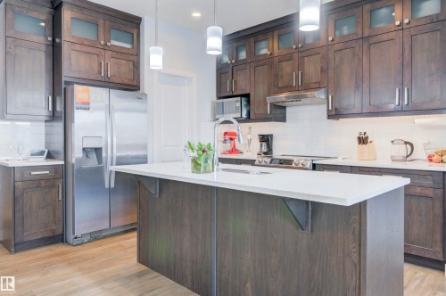 The kitchen features dark wood cabinetry, stainless steel appliances, a white subway tile backsplash, and a large island with a white countertop - 8452 Cushing Crest, Edmonton, AB - Indoor Photo Showing Kitchen With Upgraded Kitchen