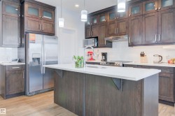 The kitchen features dark wood cabinetry, stainless steel appliances, a white subway tile backsplash, and a large island with a white countertop - 