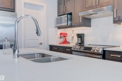 The kitchen features a double sink with a chrome faucet, light-colored countertops, dark wood cabinetry, and a stainless steel oven - 