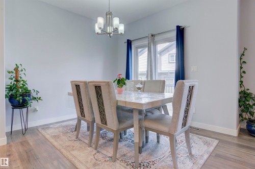 Dining area featuring hard surface flooring, a chandelier, and a large window with blue curtains - 8452 Cushing Crest, Edmonton, AB - Indoor Photo Showing Dining Room