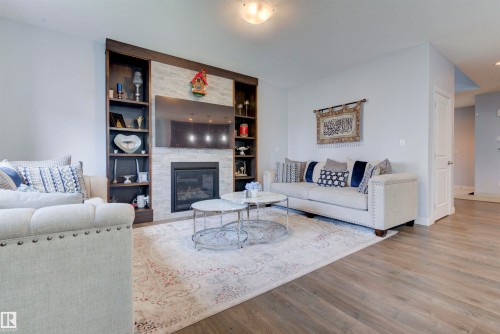 The living area features a built-in fireplace with a stone surround, integrated shelving, and hardwood flooring - 8452 Cushing Crest, Edmonton, AB - Indoor Photo Showing Living Room With Fireplace