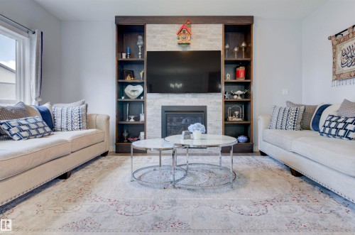 Living room featuring a fireplace with a stone facade, built-in shelving, and a large window providing natural light - 8452 Cushing Crest, Edmonton, AB - Indoor Photo Showing Living Room With Fireplace