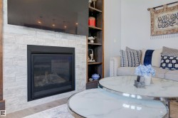 The living area features a fireplace with a light-toned stone surround, integrated shelving, and a light-colored sofa with throw pillows - 