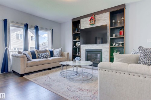 The living room features a fireplace with a stone surround, built-in shelving, and hardwood floors - 8452 Cushing Crest, Edmonton, AB - Indoor Photo Showing Living Room With Fireplace