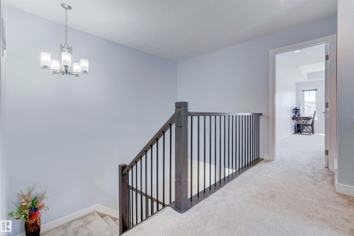 The property features a staircase with dark wood railings and black metal balusters, and a carpeted hallway - 8452 Cushing Crest, Edmonton, AB - Indoor Photo Showing Other Room