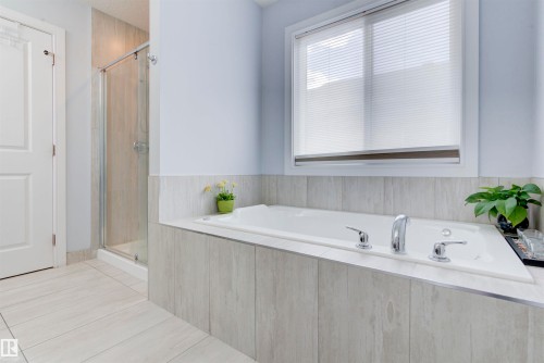 The bathroom features a built-in tub with chrome fixtures, a shower with a glass enclosure, and light-colored tiled flooring - 8452 Cushing Crest, Edmonton, AB - Indoor Photo Showing Bathroom