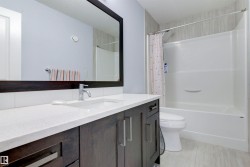 The bathroom features a vanity with a white countertop and dark wood cabinetry, a large mirror, and a white bathtub with a shower - 