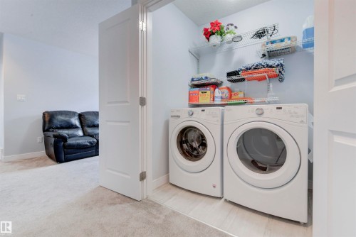 Dedicated laundry area featuring front-loading washer and dryer units, overhead wire shelving, and a light-colored tile floor - 8452 Cushing Crest, Edmonton, AB - Indoor Photo Showing Laundry Room