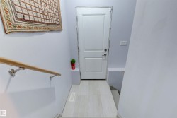 Entryway with light-colored flooring, a white door, and a wooden handrail - 