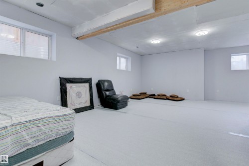 This spacious room features light-colored walls and flooring, with visible ceiling beams and recessed lighting fixtures - 8452 Cushing Crest, Edmonton, AB - Indoor