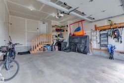 The property features a spacious garage with a concrete floor, a wooden staircase, and a white door leading into the interior - 