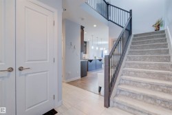 Entryway featuring light-colored tiled flooring, a carpeted staircase with dark railings, and white doors - 
