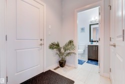 The property features a bright entrance area with white tile flooring and a well-appointed bathroom with a dark wood vanity, a mirror, and a wall-mounted light fixture - 