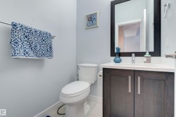 This powder room features a white toilet, a vanity with a white countertop and dark wood cabinetry, and a framed mirror - 
