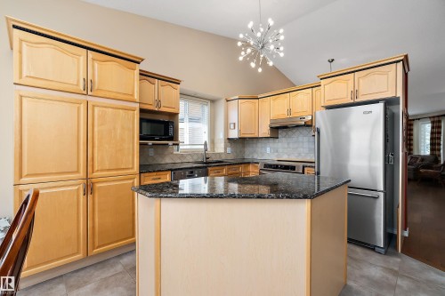 The kitchen features light wood cabinetry, a central island with a granite countertop, and stainless steel appliances - 14 920 119 Street, Edmonton, AB - Indoor Photo Showing Kitchen