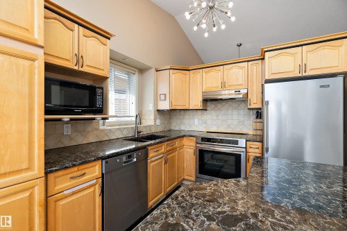 Kitchen featuring light wood cabinetry, dark marbled countertops, stainless steel appliances, and a tiled backsplash - 14 920 119 Street, Edmonton, AB - Indoor Photo Showing Kitchen With Double Sink