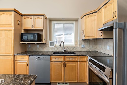 The kitchen features wood cabinetry, a stainless steel dishwasher, a black microwave, and a black sink with a gooseneck faucet - 14 920 119 Street, Edmonton, AB - Indoor Photo Showing Kitchen